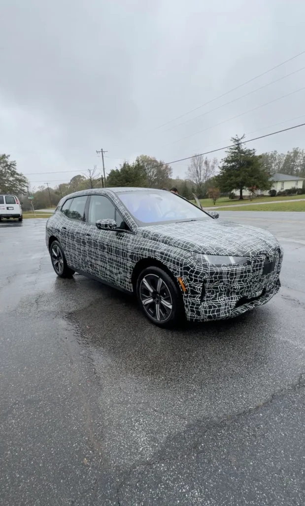 El BMW iX 2025 en vista 3/4: su camuflaje oculta las líneas finales de diseño, mientras promete una evolución aerodinámica sobresaliente.