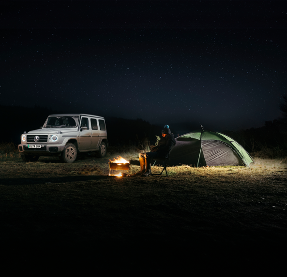 Bajo la fría noche, el fuego ilumina la escena mientras nuestro compañero y el Mercedes G 580 EQ comparten la esencia de la aventura: libertad y resistencia.