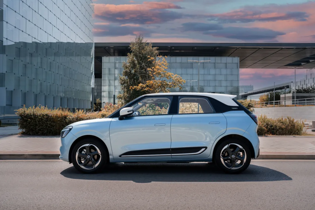 Vista lateral del Dongfeng BOX blanco perla circulando por el centro de Madrid, destacando su diseño minimalista y etiqueta Cero de la DGT