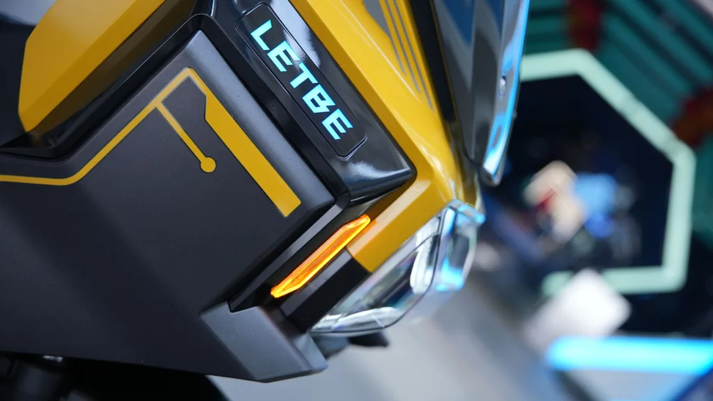 Un primer plano estático de la LETBE Mecha 125 en color Amarillo Ettore, destacando su óptica delantera LED agresiva, carenados angulosos ciberpunk y el baúl premium trasero forrado en tela